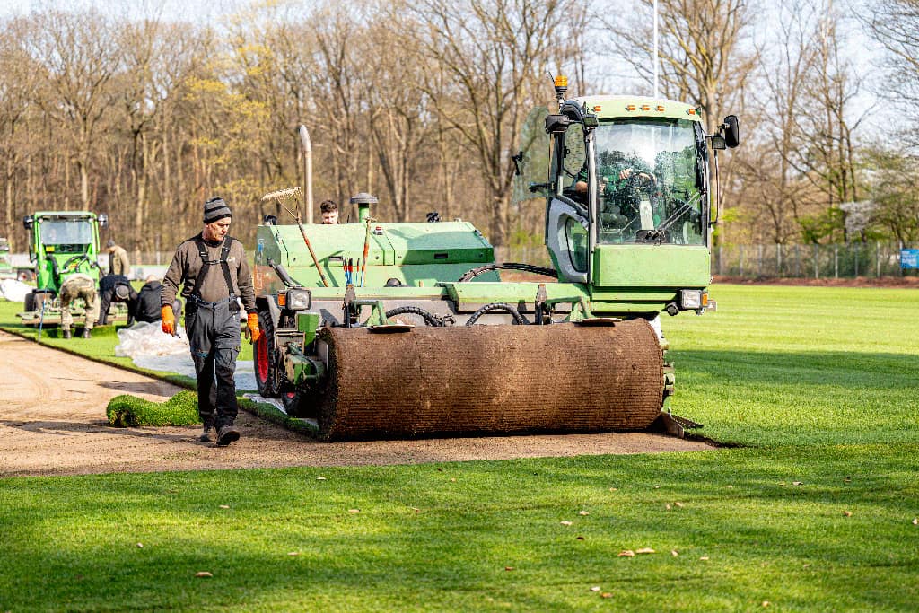 Rollrasen wird mit einer Großrollen-Maschine auf einer Sportanlage verlegt